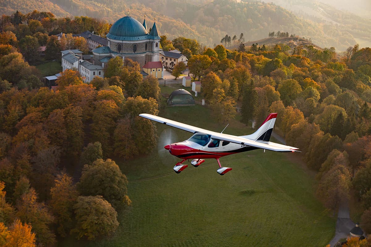 Bristell B8M flying past a hilltop church in autumn