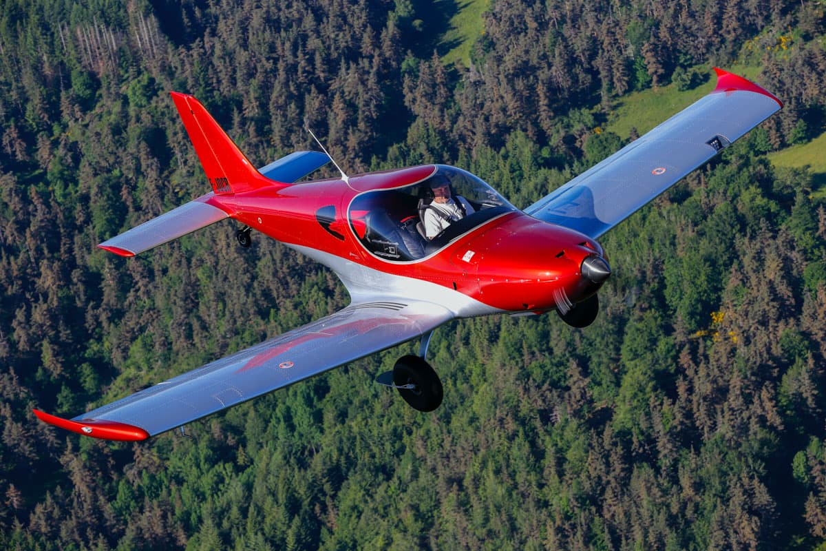 Red-and-white Bristell TDO banking over forest